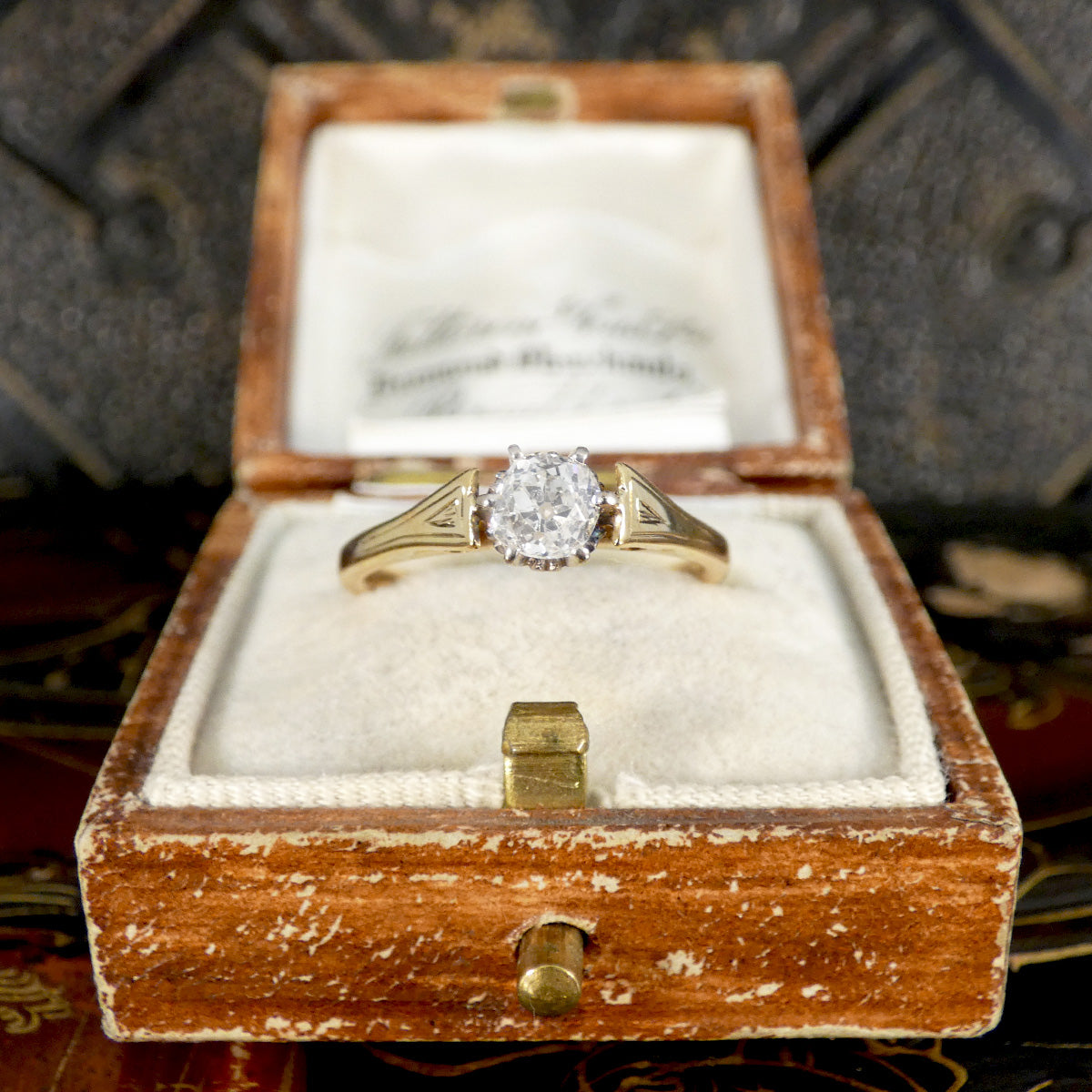 Gold ring with a diamond in an open wooden box on a patterned surface