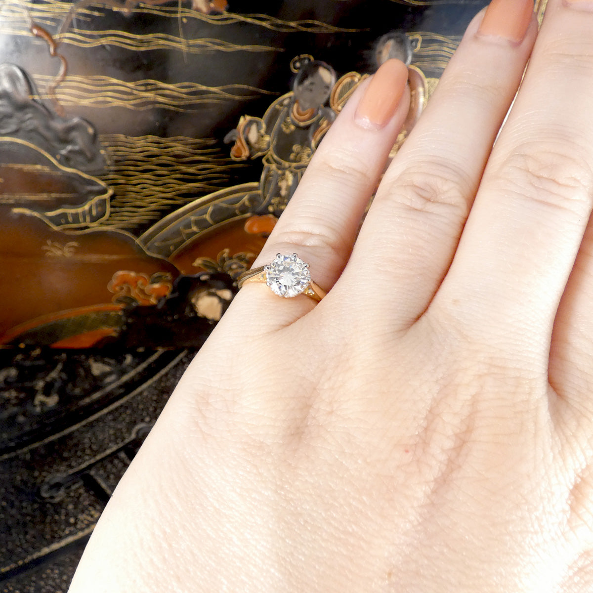 Hand wearing a diamond ring with an ornate background