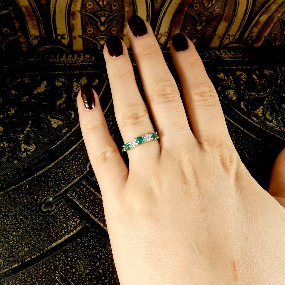 Featuring bright and vibrant emeralds sandwiching bright and clear diamonds in a five stone band ring. Showcasing ring on a finger for size reference.