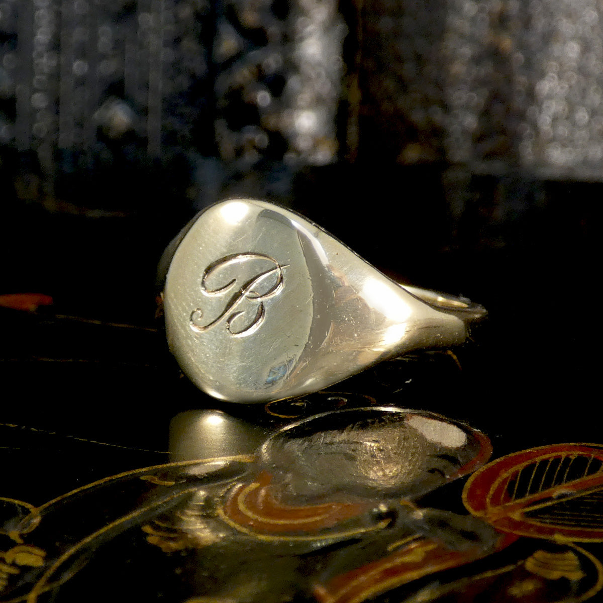 Gold ring with an engraved letter 'B' on a reflective surface