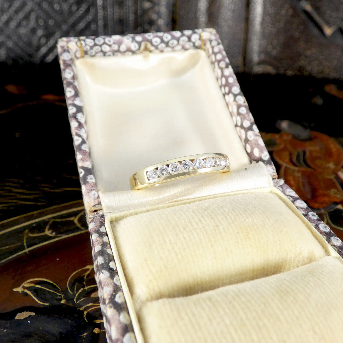 Gold ring with diamonds in an open jewelry box on a decorative background