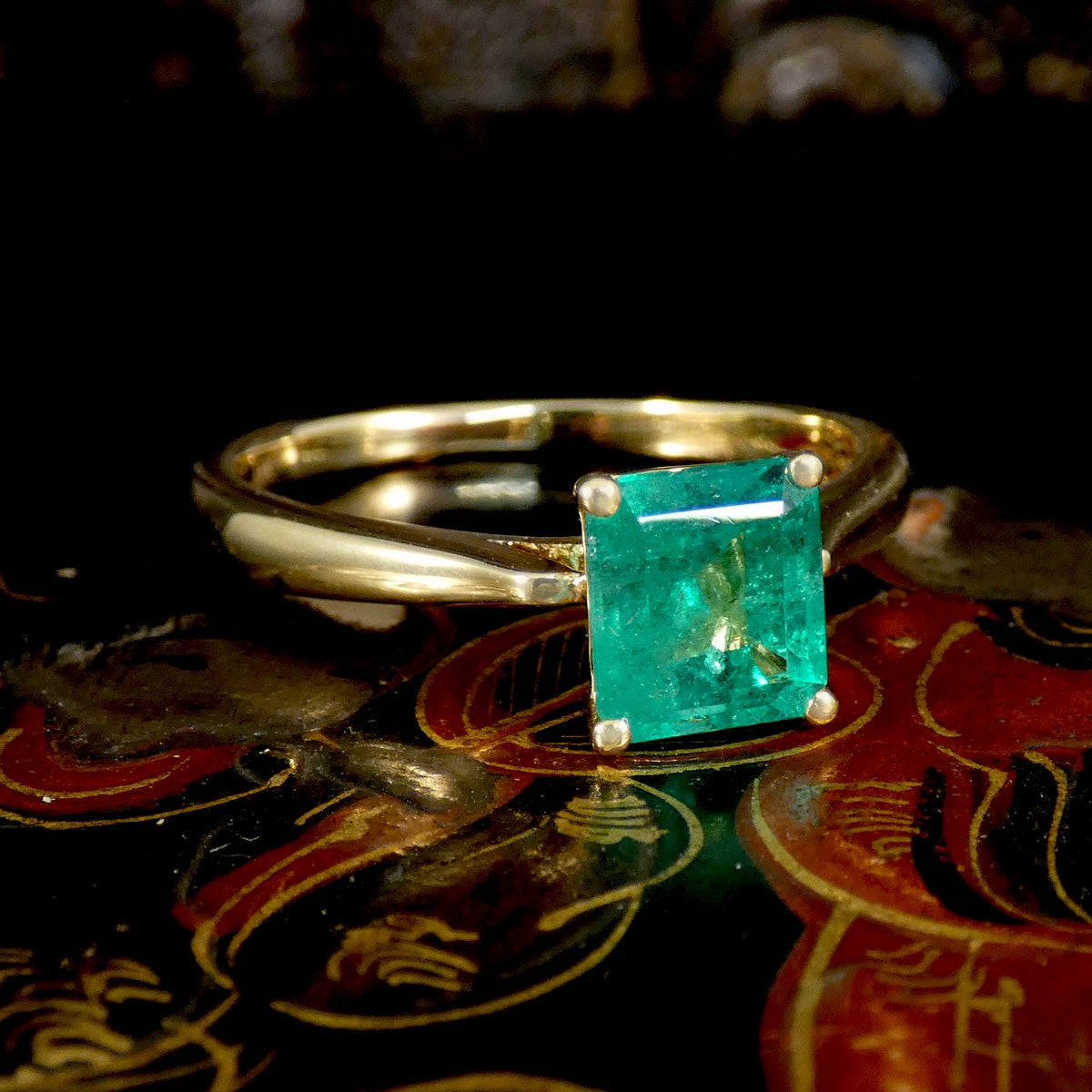 Gold ring with a green gemstone on a decorative surface