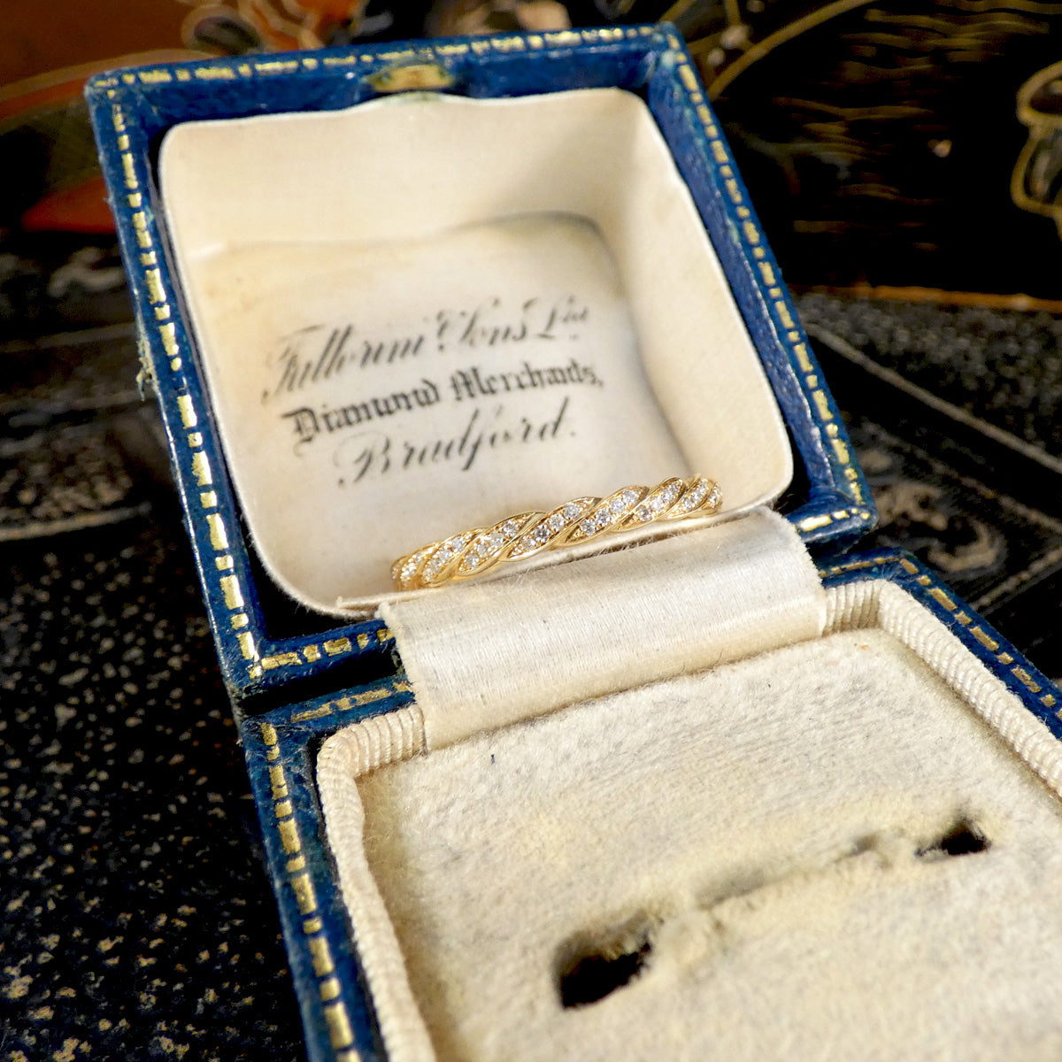 Gold ring with diamonds in an open jewelry box on a patterned surface