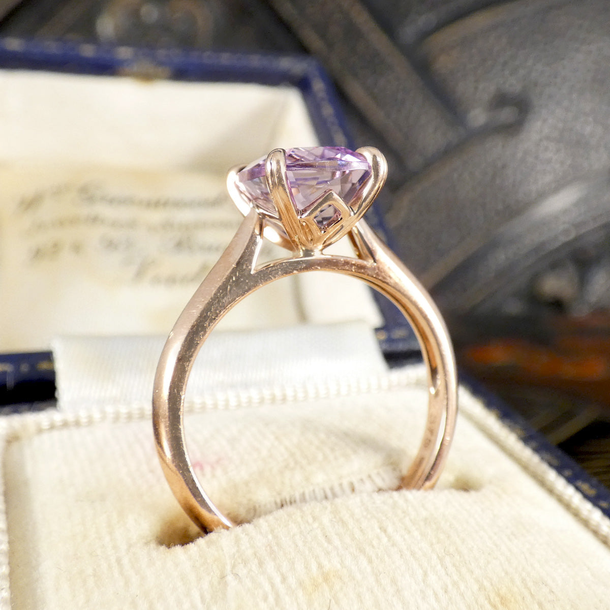 Rose gold ring with a purple gemstone on a textured surface
