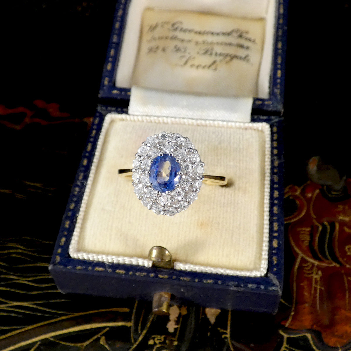 Vintage-style blue sapphire and diamond cluster ring presented in a navy blue antique ring box with cream velvet interior.