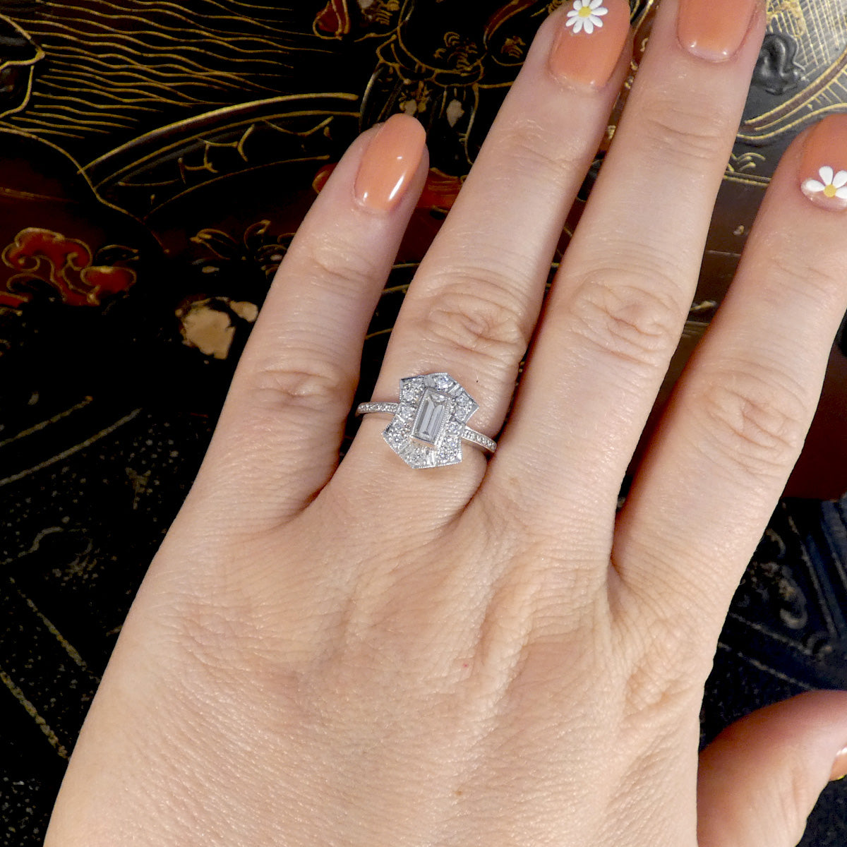 Hand wearing a diamond ring with a decorative background