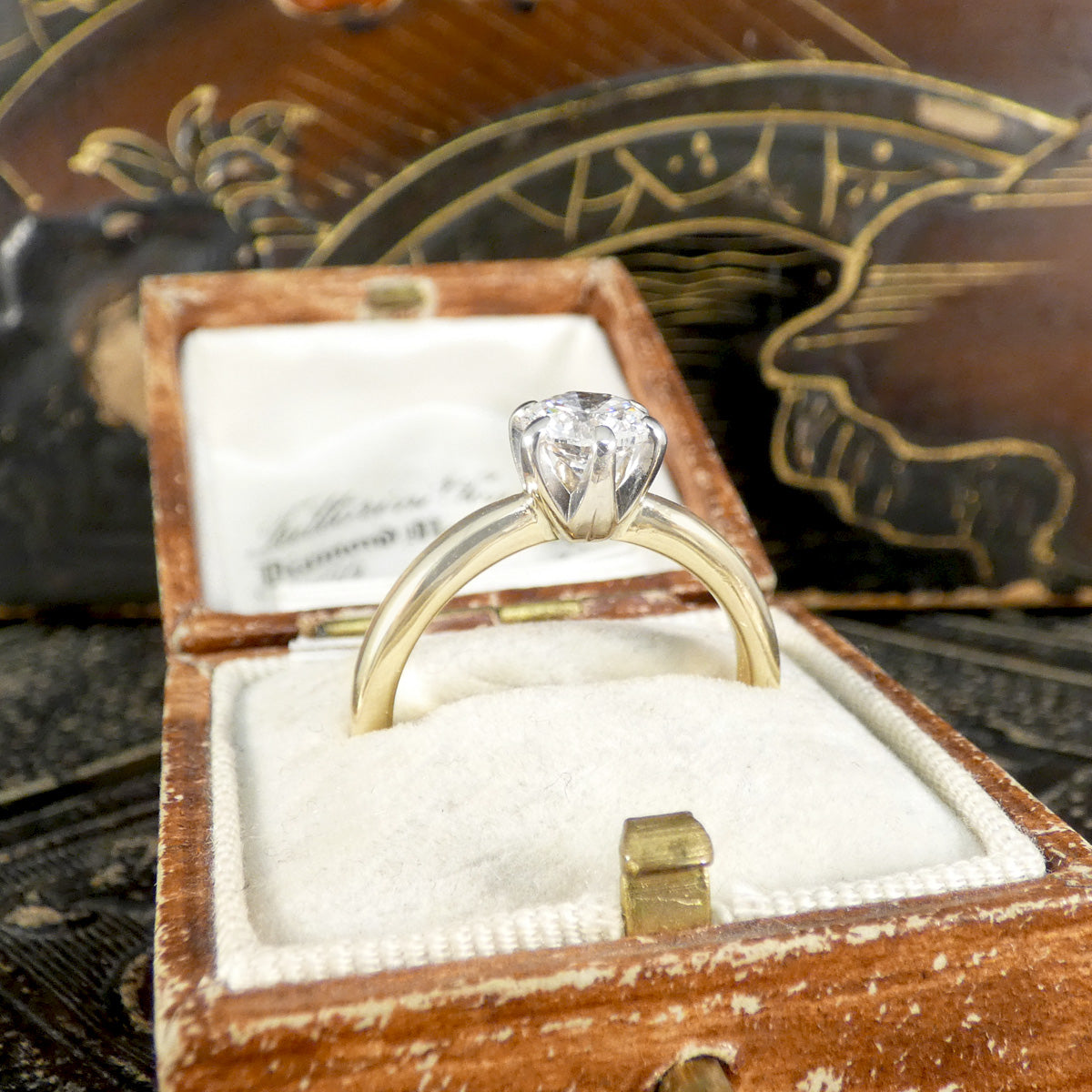 Gold diamond ring in an open wooden box with a decorative background
