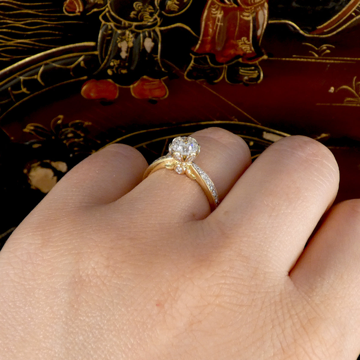 Gold ring with a diamond on a person's finger against a decorative background
