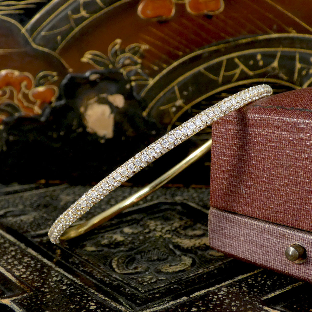 Gold bracelet with diamonds on a decorative surface next to a jewelry box