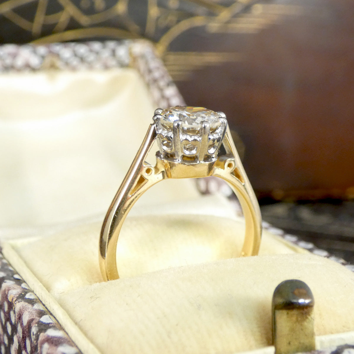 Gold ring with a diamond in a detailed basket setting, sitting in a jewellery box