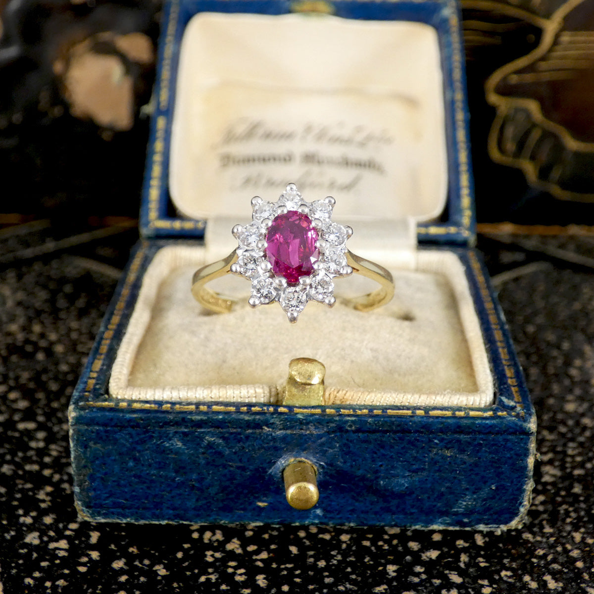 Gold ring with a ruby gemstone and a diamond surround in a blue velvet box