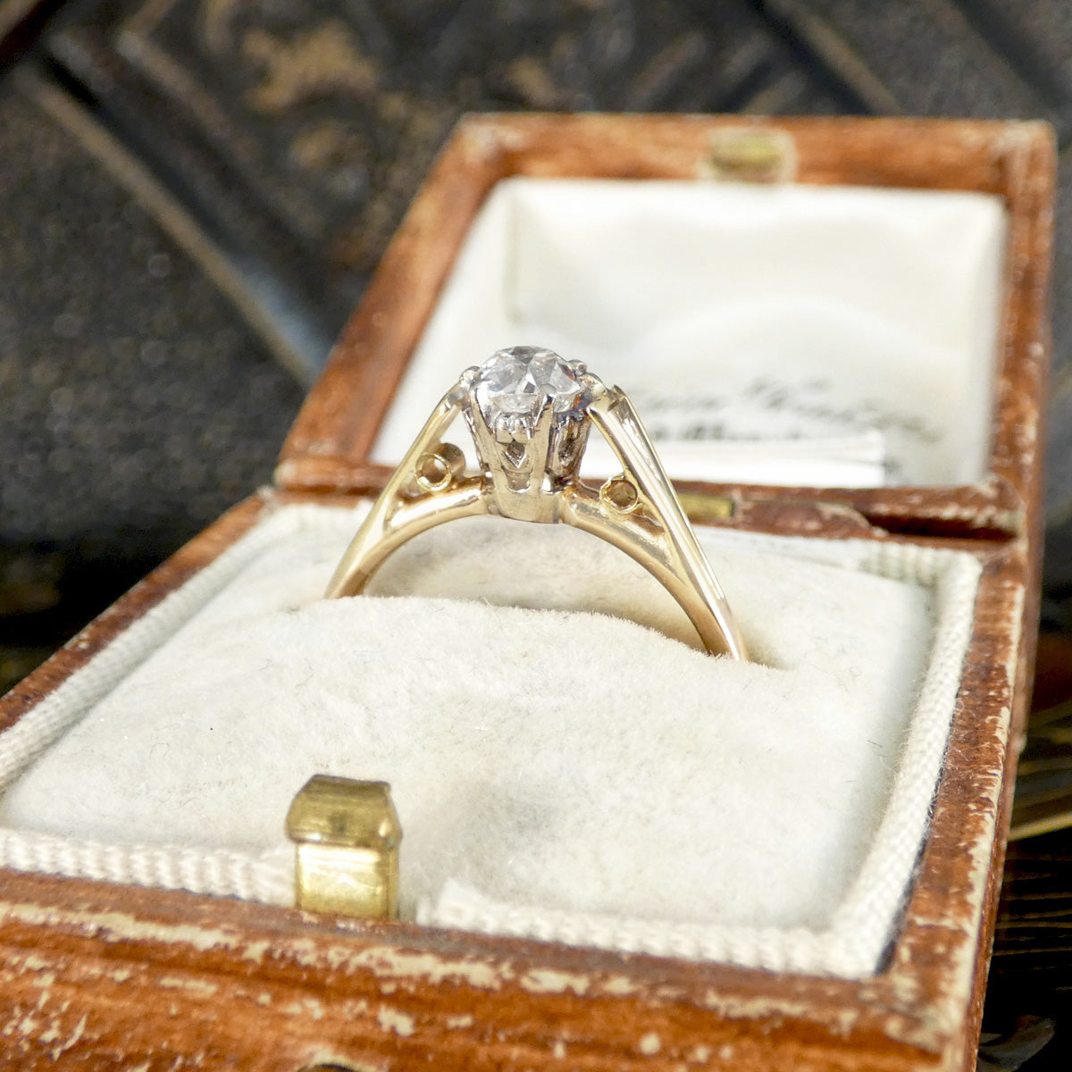 Gold diamond ring in a wooden jewelry box with a textured background