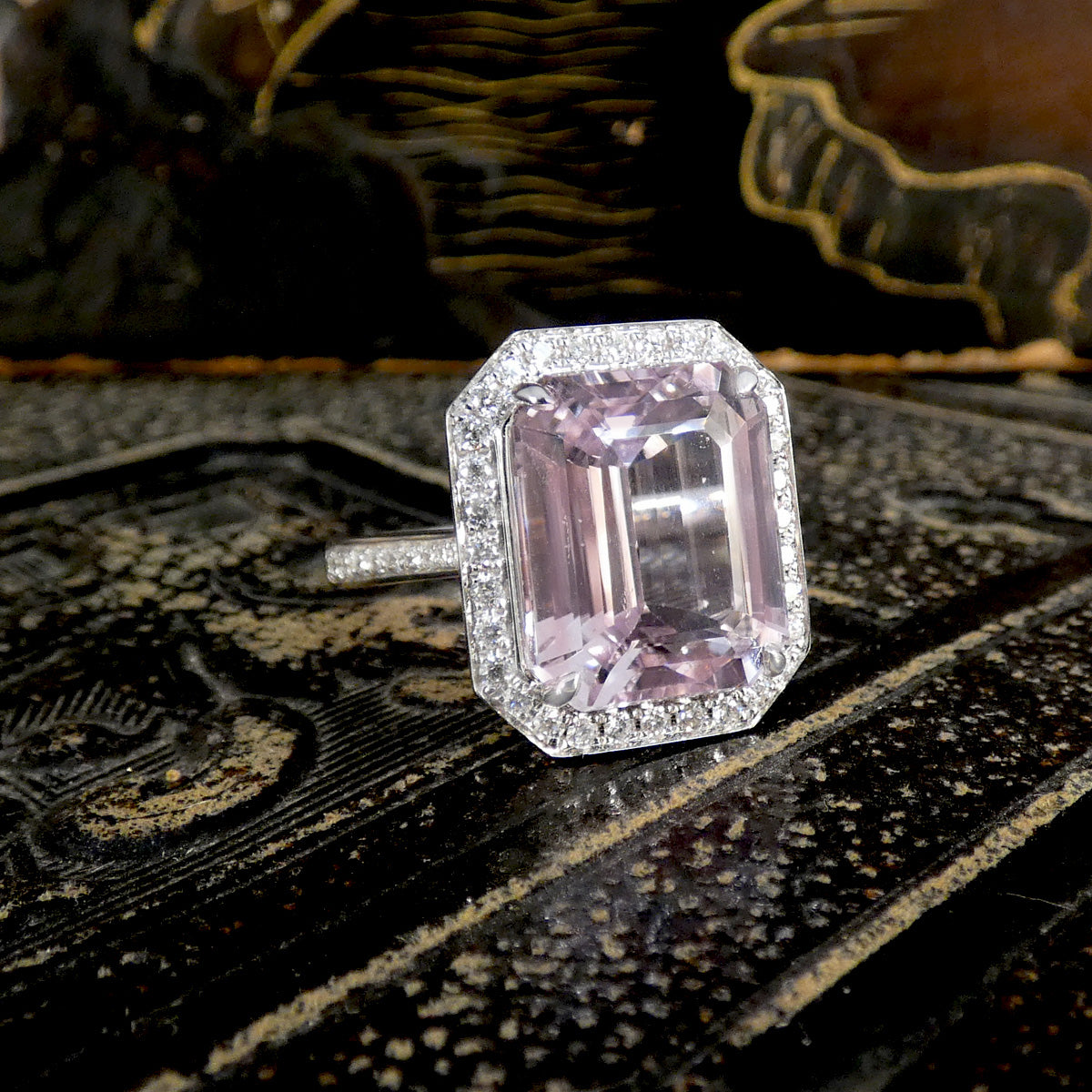 Pink gemstone ring with diamond accents on a decorative surface