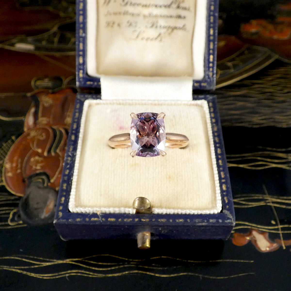 Jewelry box with a purple gemstone and gold ring on a decorative surface