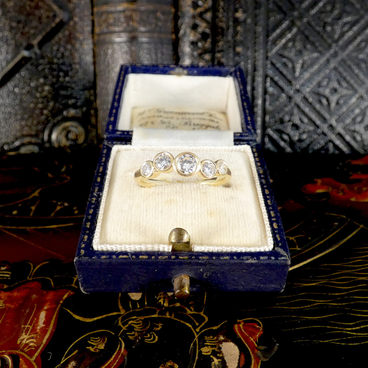 A yellow gold four-stone ring with round clear diamond gemstones, presented in an open vintage blue velvet ring box with a cream lining.