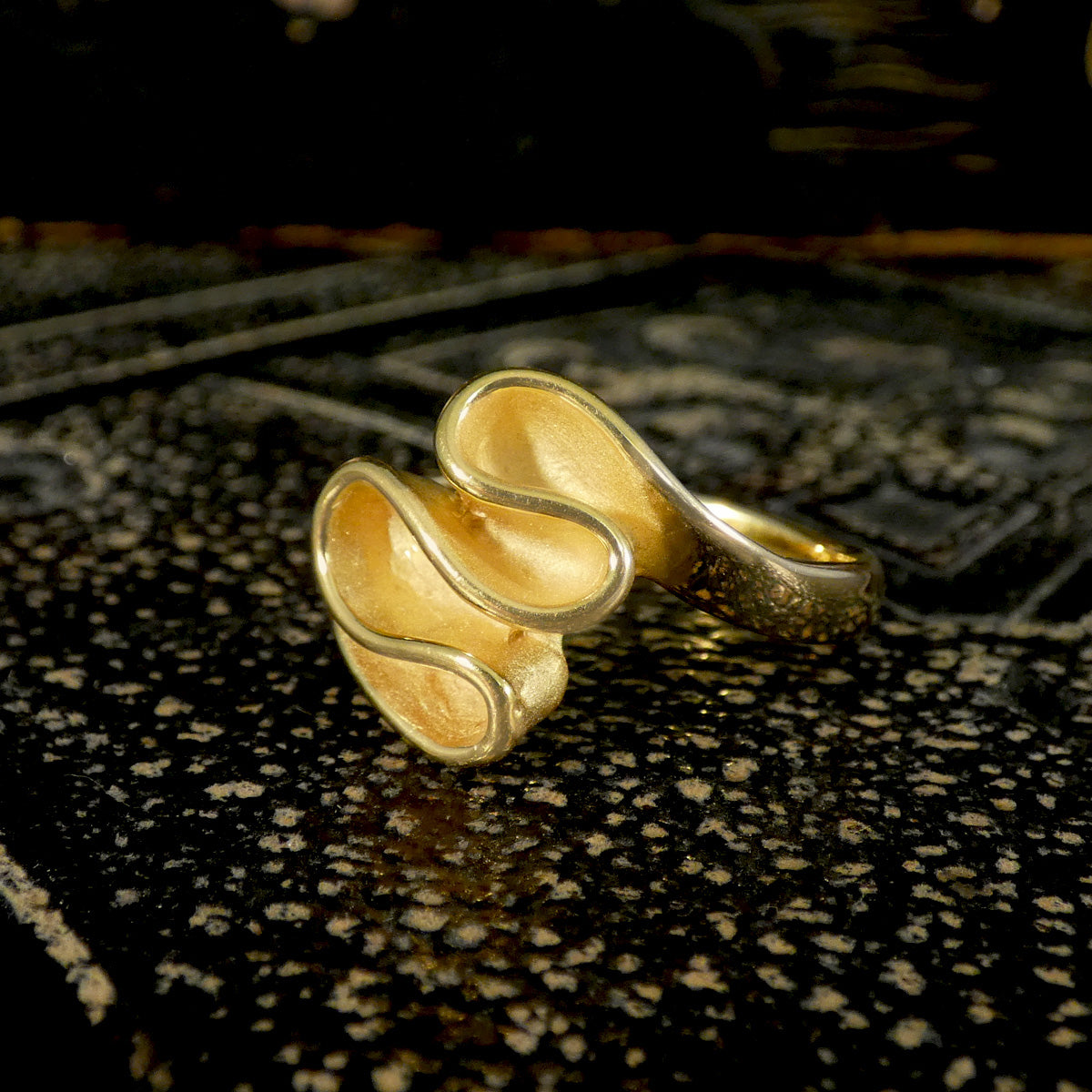 Gold ring with a textured design on a dark surface