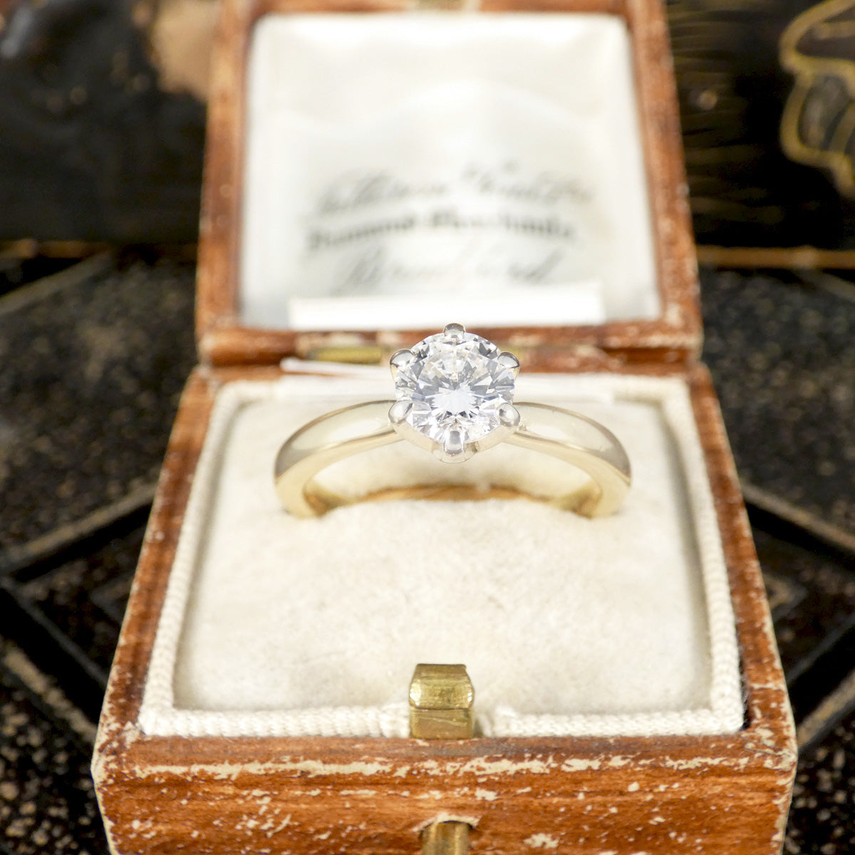 Gold ring with a diamond in a wooden box on a textured surface