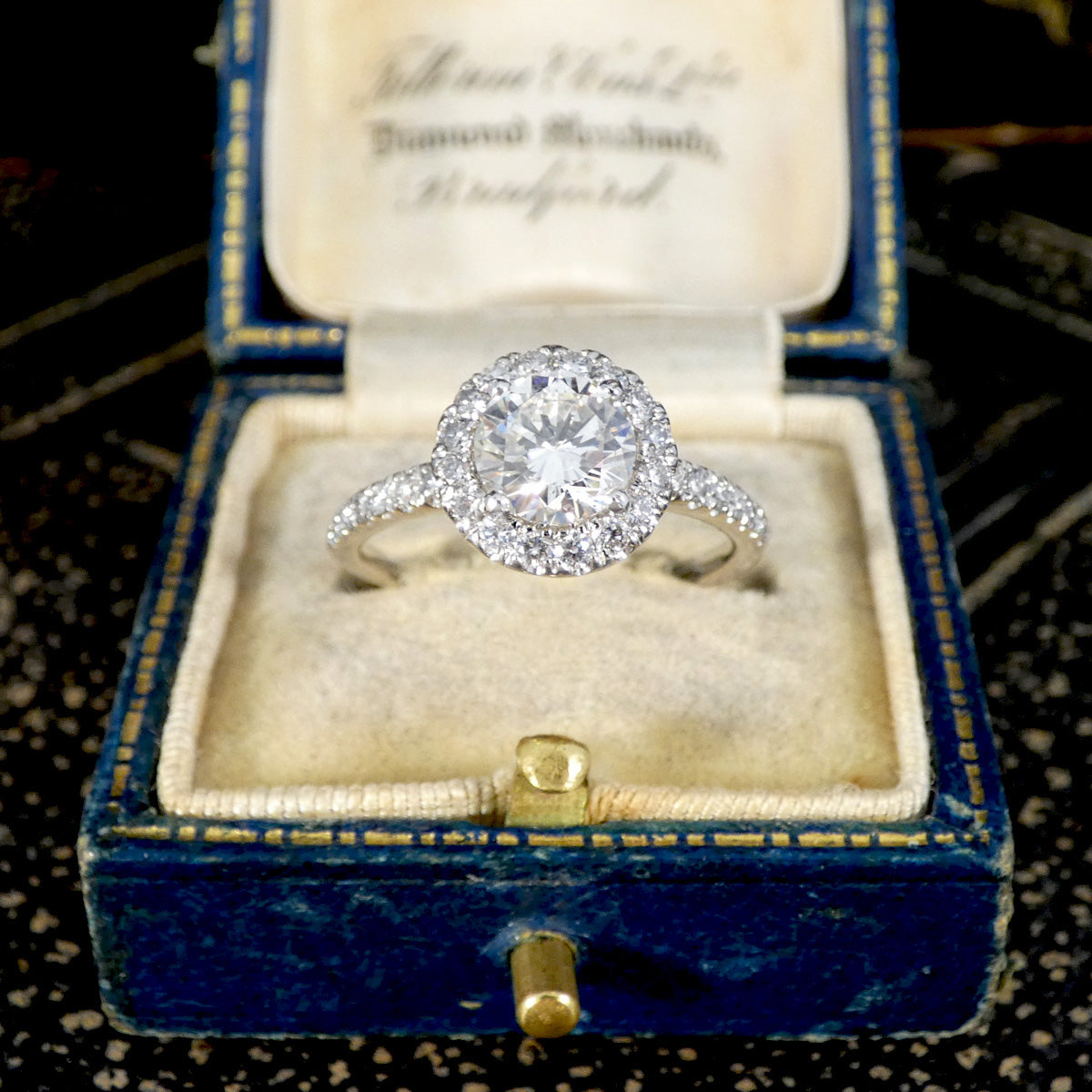 Diamond ring in an open blue velvet box with gold accents on a dark background