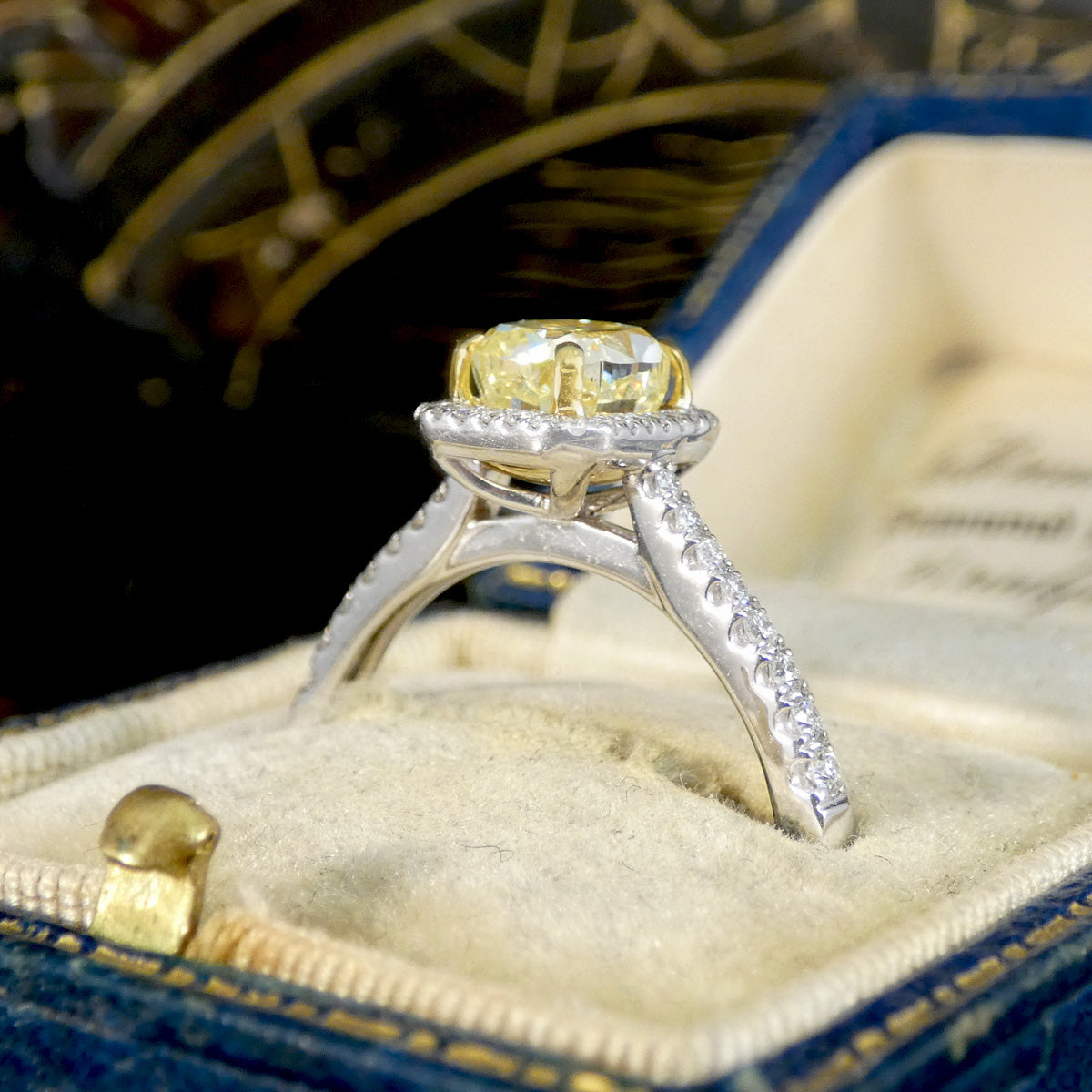 Cushion cut yellow diamond ring with a white diamond cluster halo and diamond shoulders.
