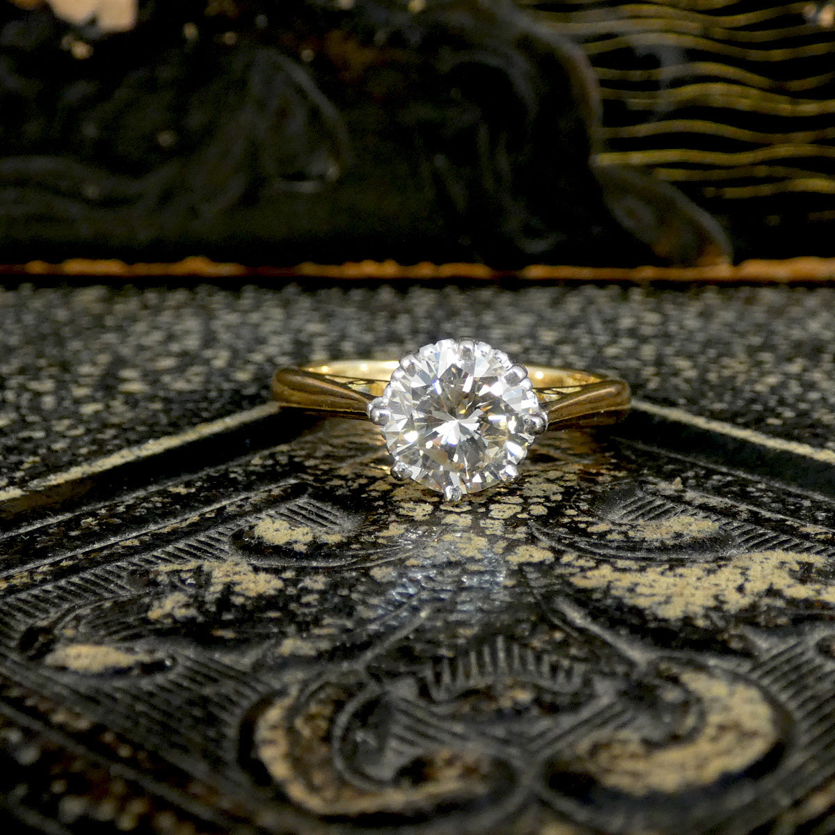 Gold solitaire ring with a diamond on an ornate surface