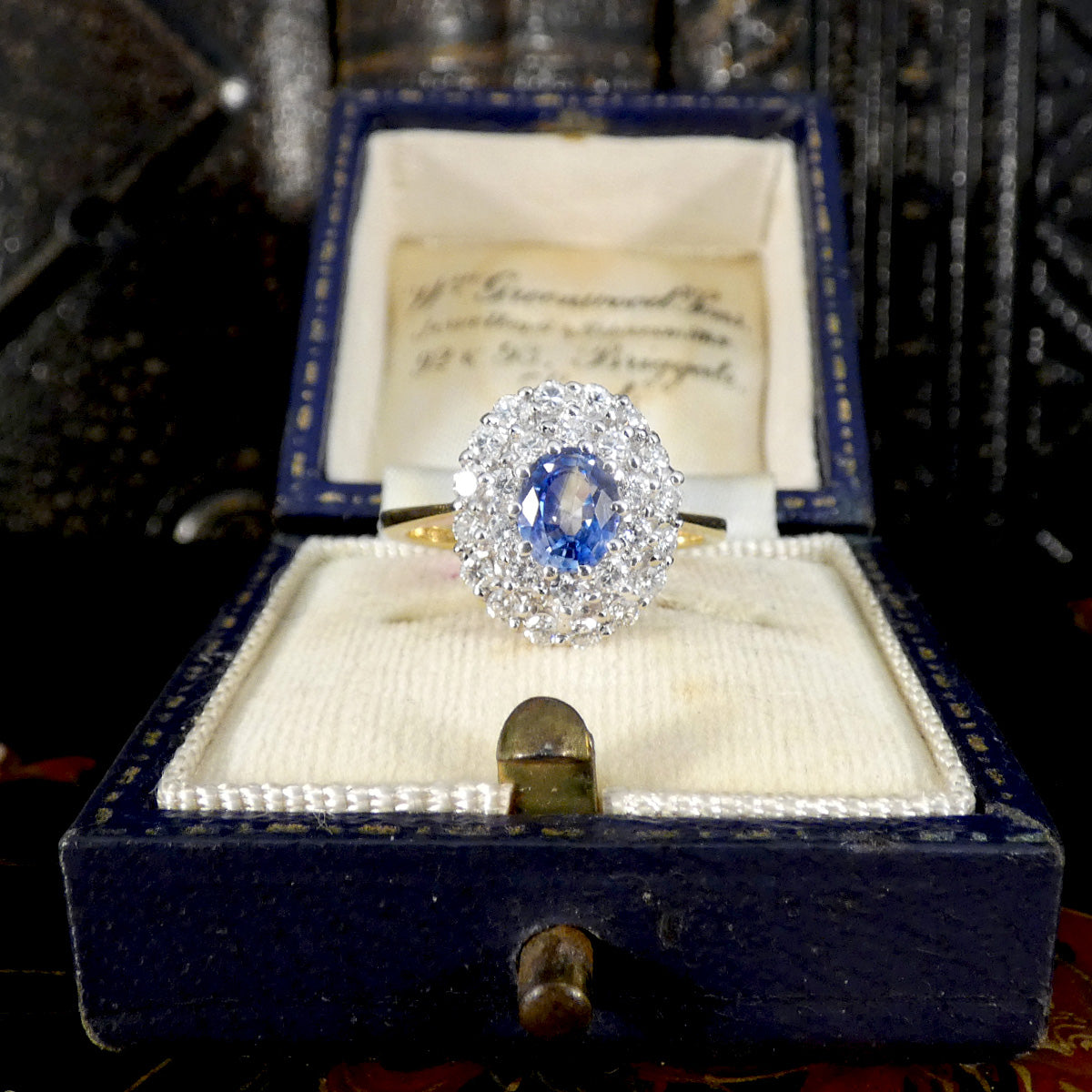 Vintage-style blue sapphire and diamond cluster ring presented in a navy blue antique ring box with cream velvet interior.