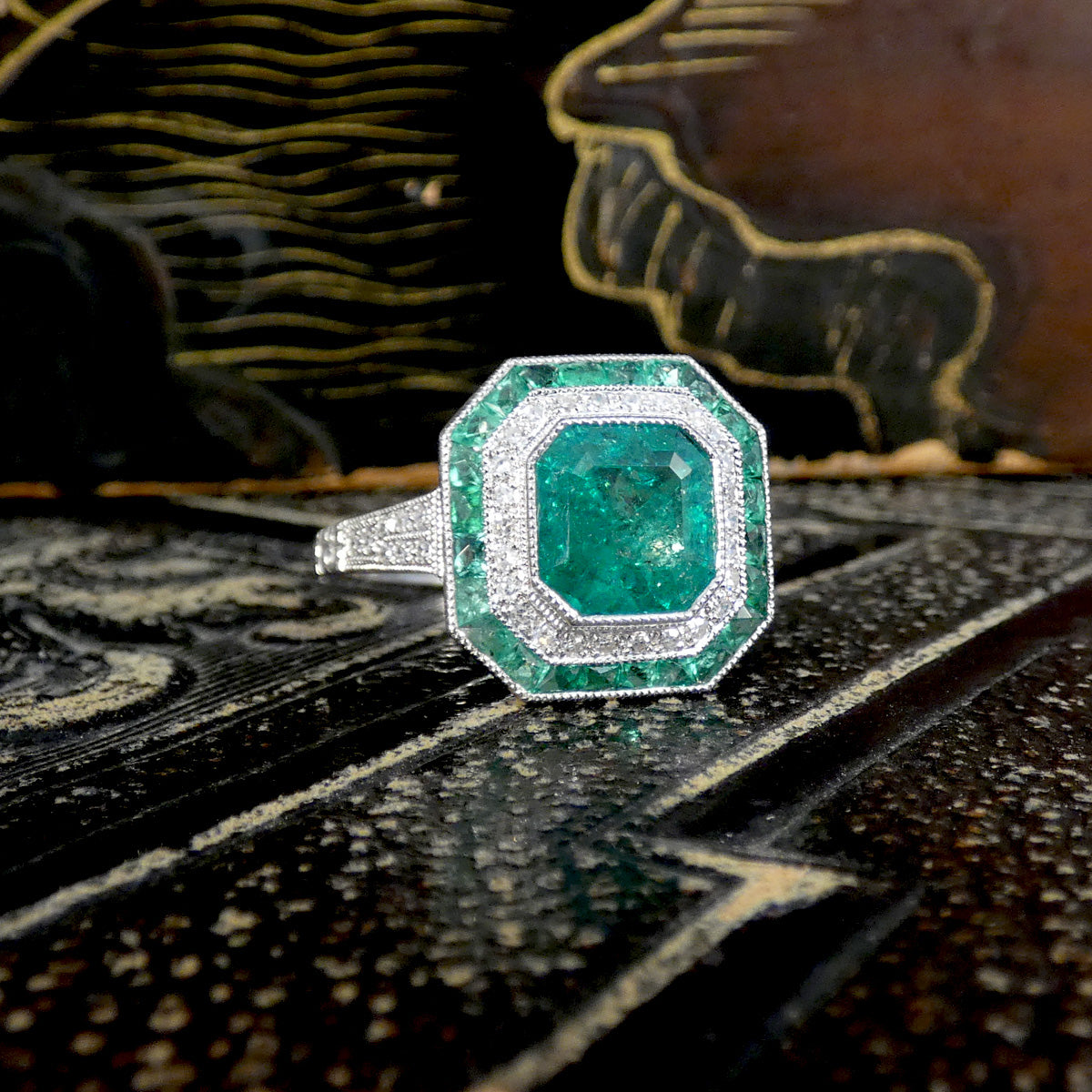 The perfect gift for any green lover. Striking Art Deco-style ring featuring a central emerald-cut emerald, surrounded by a double halo of calibre-cut emeralds and pavé-set diamonds, all set in platinum.