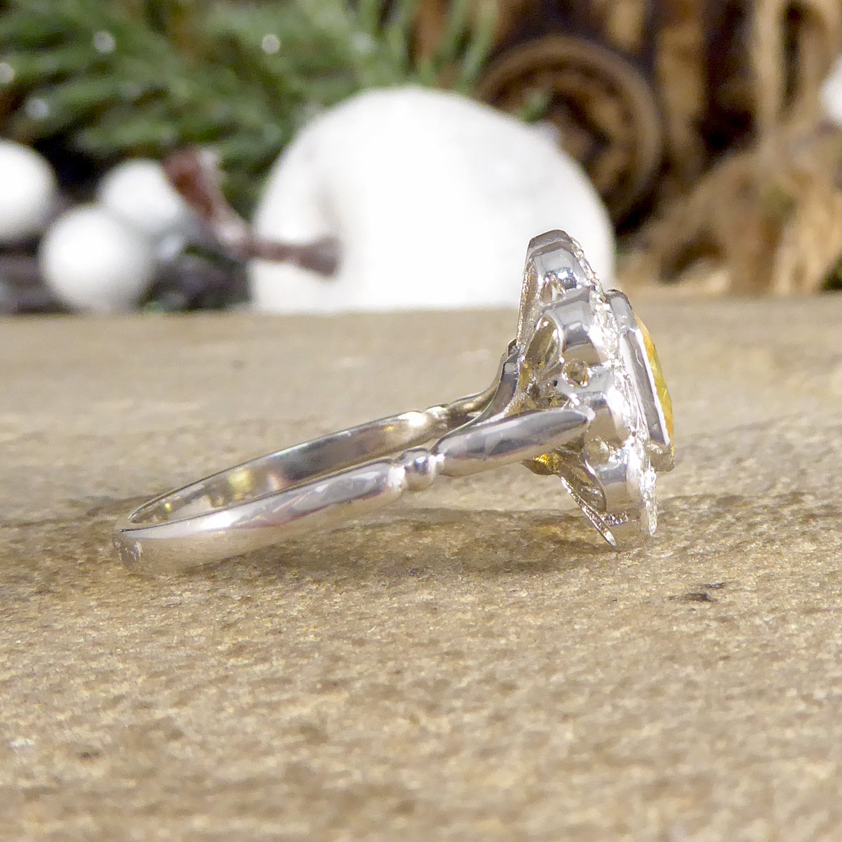 Side profile of Art Deco-style ring featuring a stunning 2.10ct Asscher cut yellow sapphire, encircled by sparkling diamonds in a timeless cluster design. Showing knotch design on the shoulder.