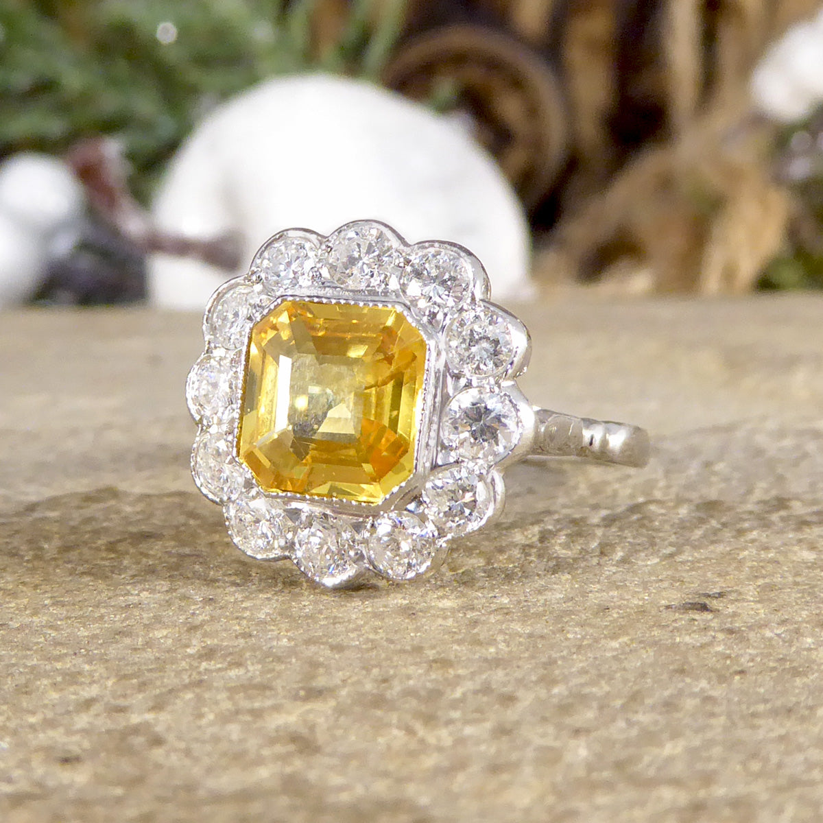 Art Deco-style ring featuring a stunning 2.10ct Asscher cut yellow sapphire, encircled by sparkling diamonds in a timeless cluster design.