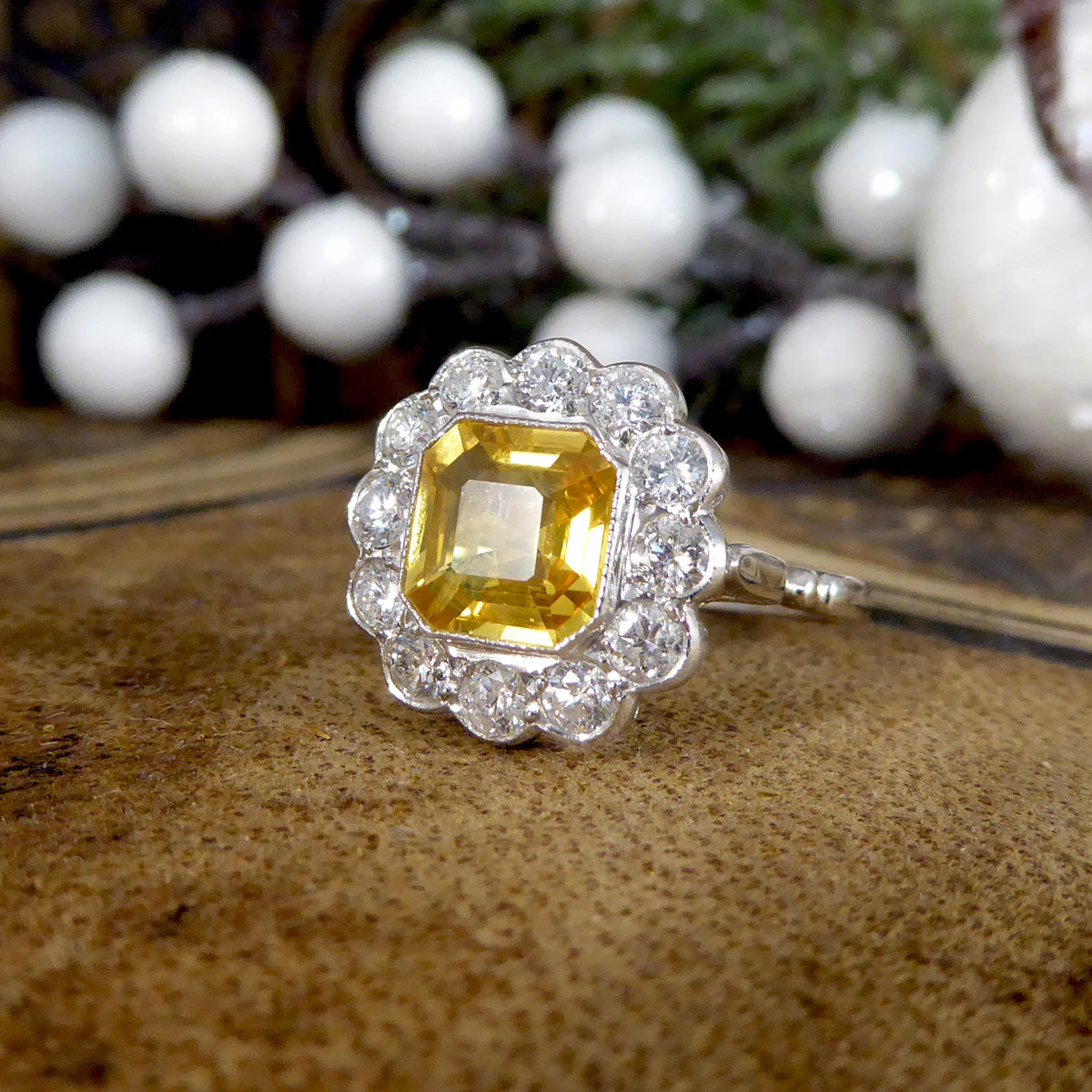 Art Deco-style ring featuring a stunning 2.10ct Asscher cut yellow sapphire, encircled by sparkling diamonds in a timeless cluster design.