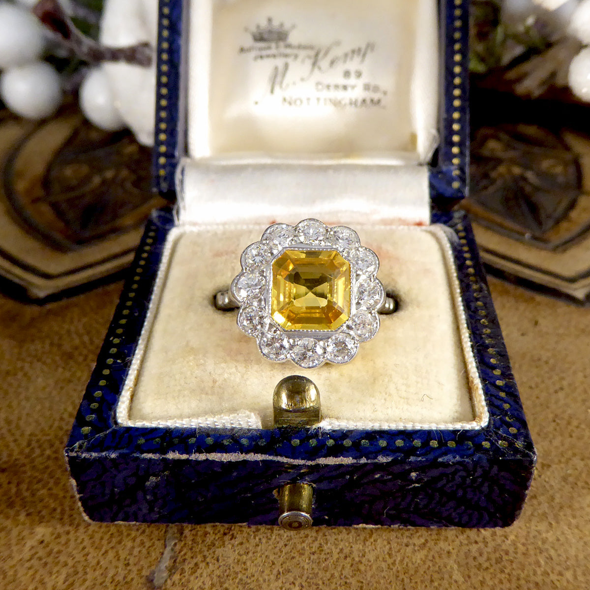 Elegant 2.10ct Asscher cut yellow sapphire and diamond cluster ring in an Art Deco-inspired design, displayed in an antique blue velvet ring box for a vintage charm.