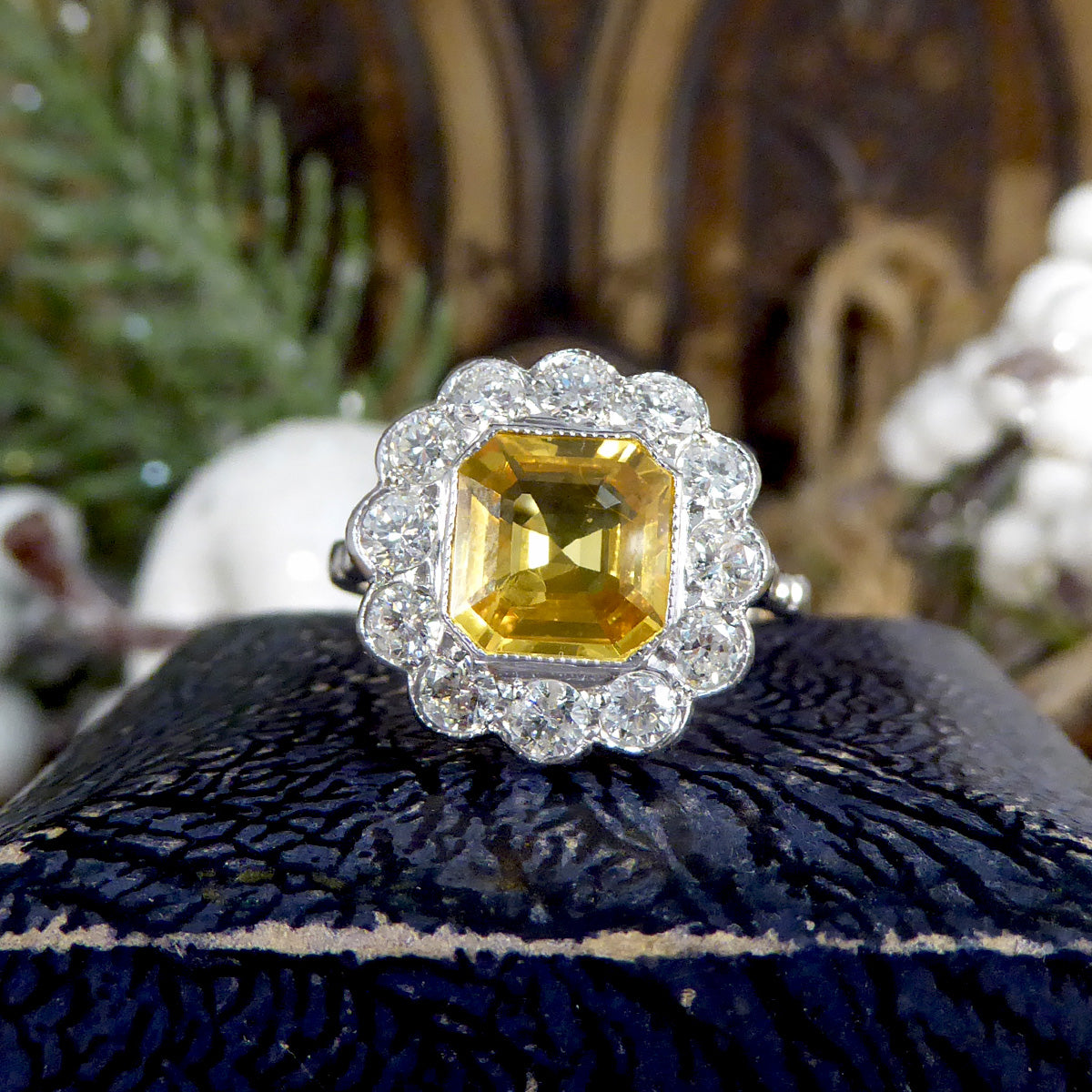 Elegant 2.10ct Asscher cut yellow sapphire and diamond cluster ring in an Art Deco-inspired design, displayed on an antique blue velvet ring box for a vintage charm. Showing vibrant yellow colour.