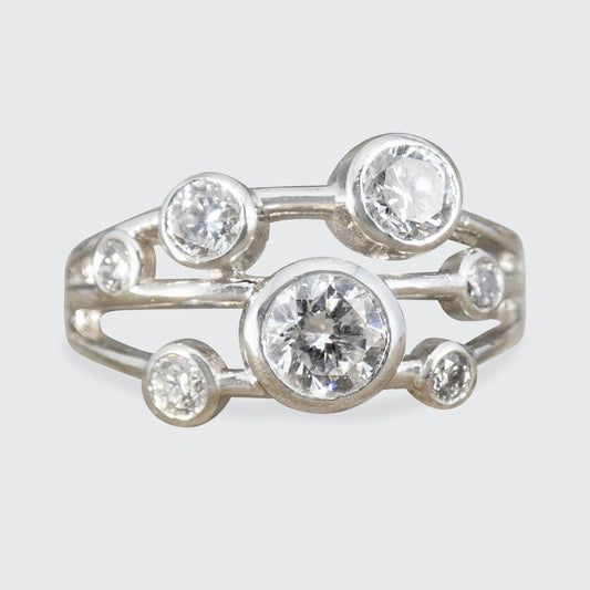 A platinum ring featuring a cluster of round clear gemstones in bezel settings, photographed against a light gray background.