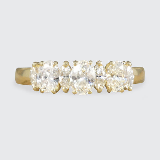 A yellow gold diamond ring with three oval brilliant-cut diamonds in a prong setting, shown against a light gray background.