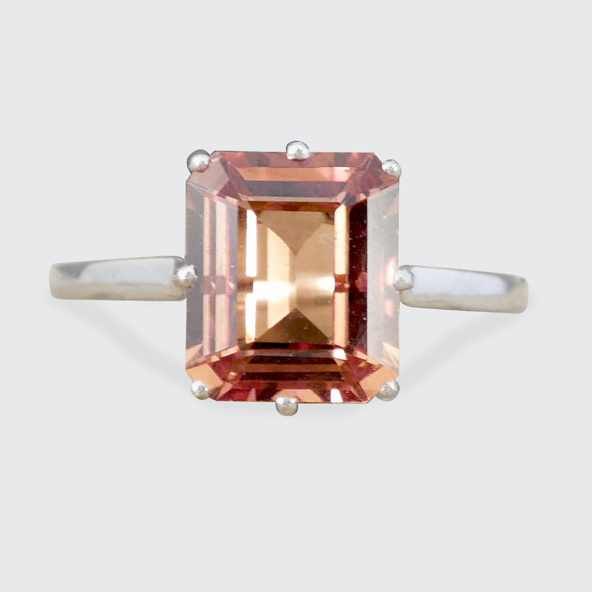 An emerald-cut orange gold gemstone ring with a silver-toned band, shown against a light gray background.