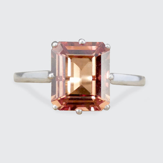 An emerald-cut orange gold gemstone ring with a silver-toned band, shown against a light gray background.