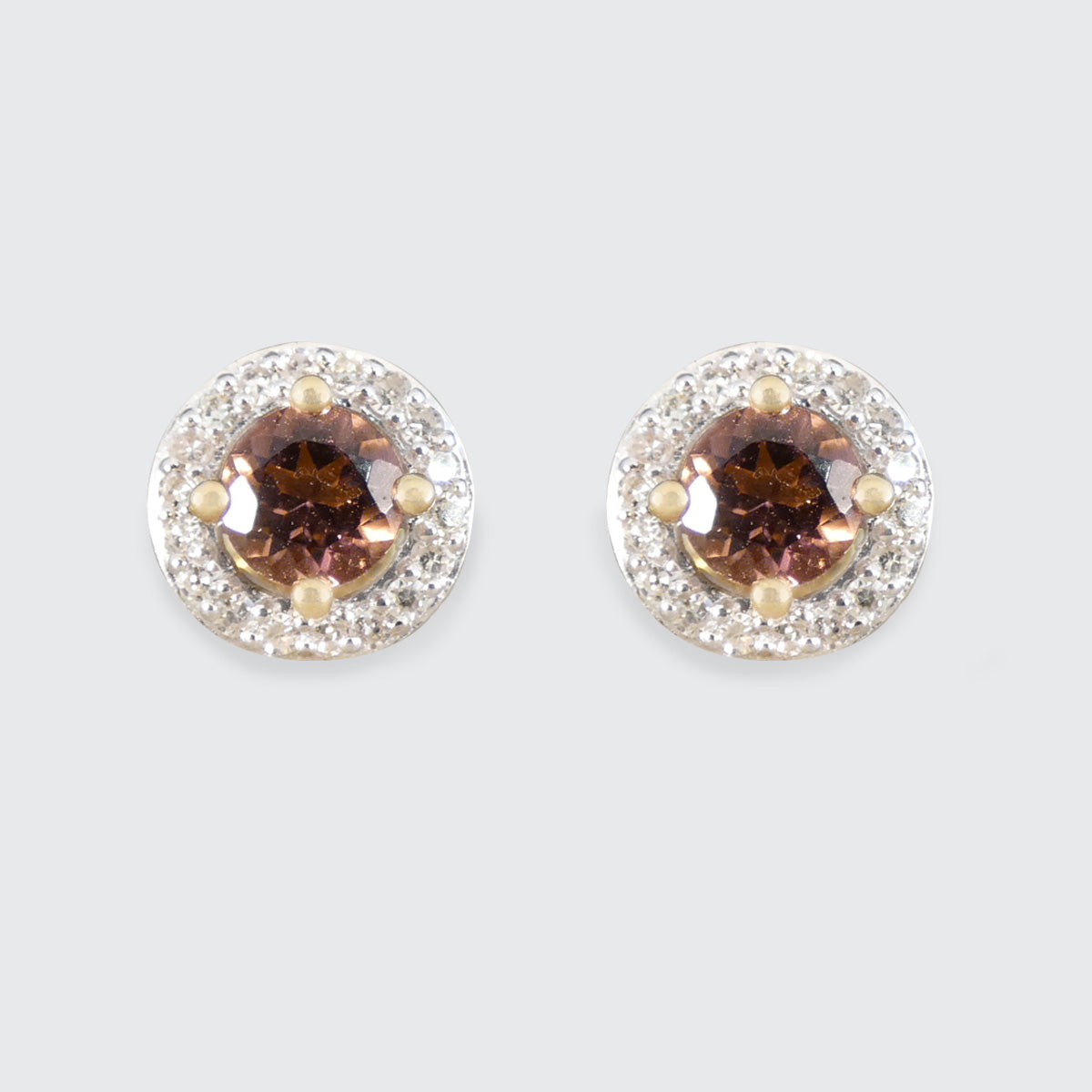 Pair of round earrings with pink gemstones and silver halo on a white background