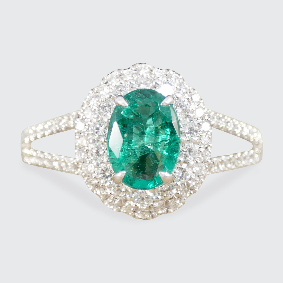 Ring with a green Emerald gemstone and diamond-studded halo on a light gray background
