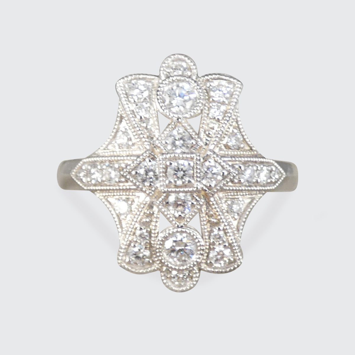 An ornate Art Deco style diamond ring featuring a symmetrical starburst design with multiple round and oval diamonds set in a silver-toned metal band, shown against a light gray background.
