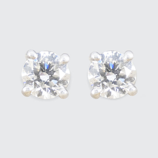 Pair of diamond stud earrings on a light grey background. 