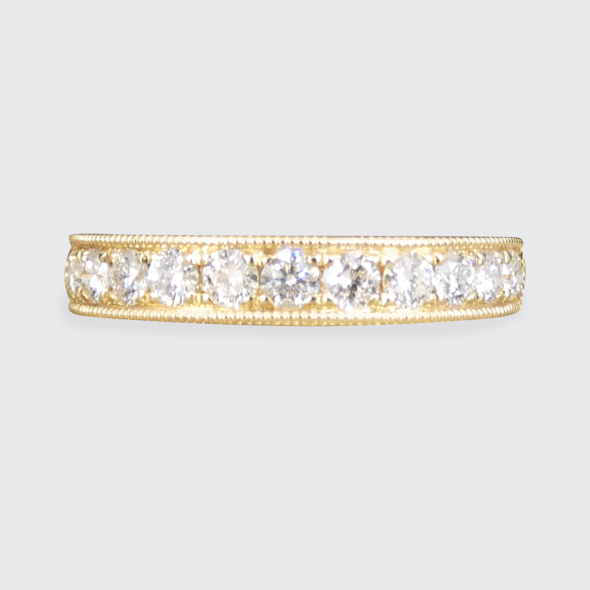A yellow gold eternity ring featuring a row of round-cut clear gemstones, set against a light gray background.