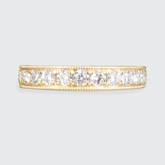 A yellow gold eternity ring featuring a row of round-cut clear gemstones, set against a light gray background.