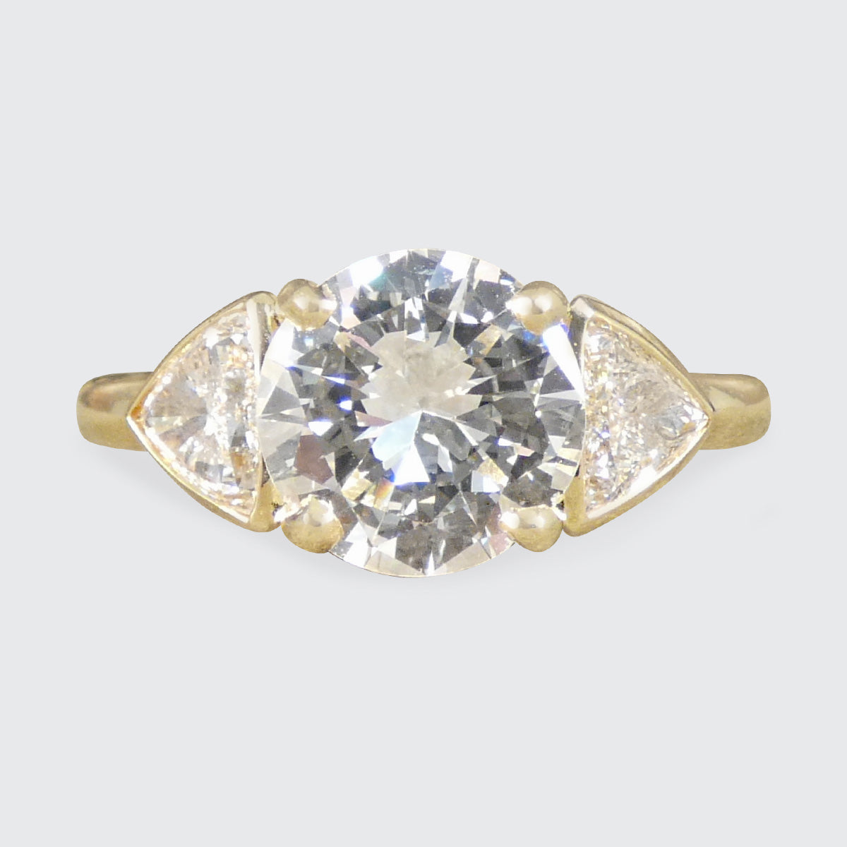 Gold ring with a large diamond and smaller diamonds on the sides against a light gray background