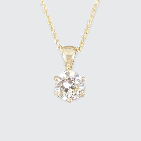 A yellow gold solitaire necklace featuring a round-cut clear diamond pendant in a prong setting, suspended from a delicate gold chain against a light gray background.