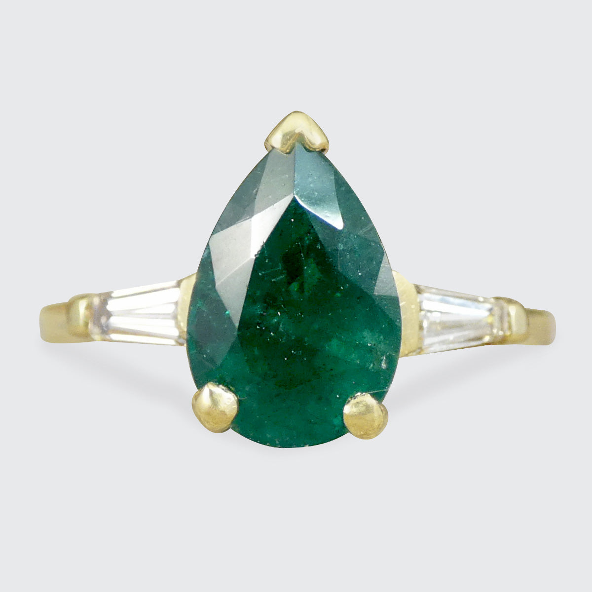 Gold ring with a green teardrop-shaped Emerald gemstone on a light gray background