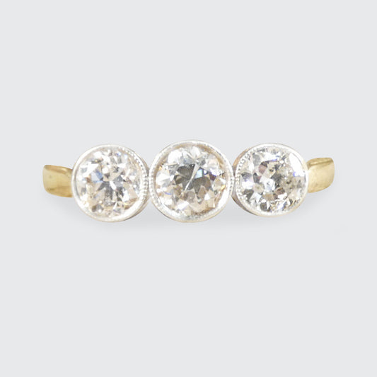 Three-stone diamond ring with gold setting on a light gray background