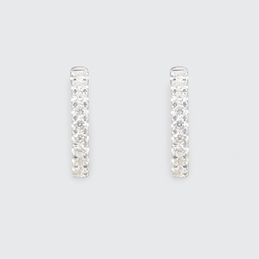A pair of silver-toned huggie hoop earrings paved with clear cubic zirconia stones, shown against a solid light gray background.
