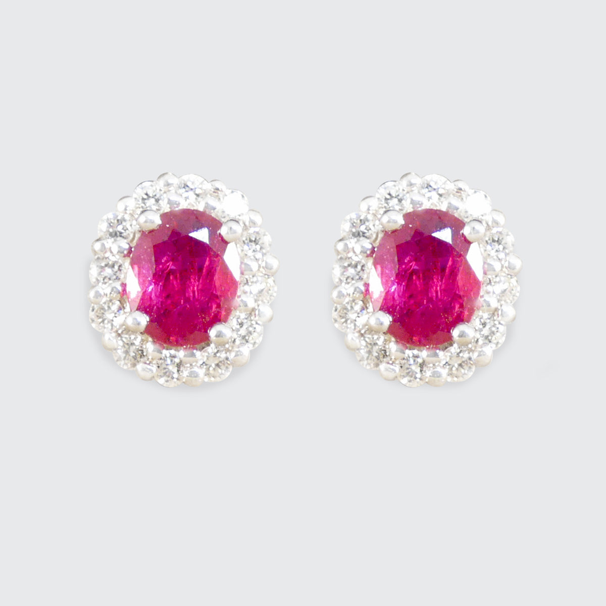 Pair of earrings with pink ruby gemstones and silver surrounds on a light gray background