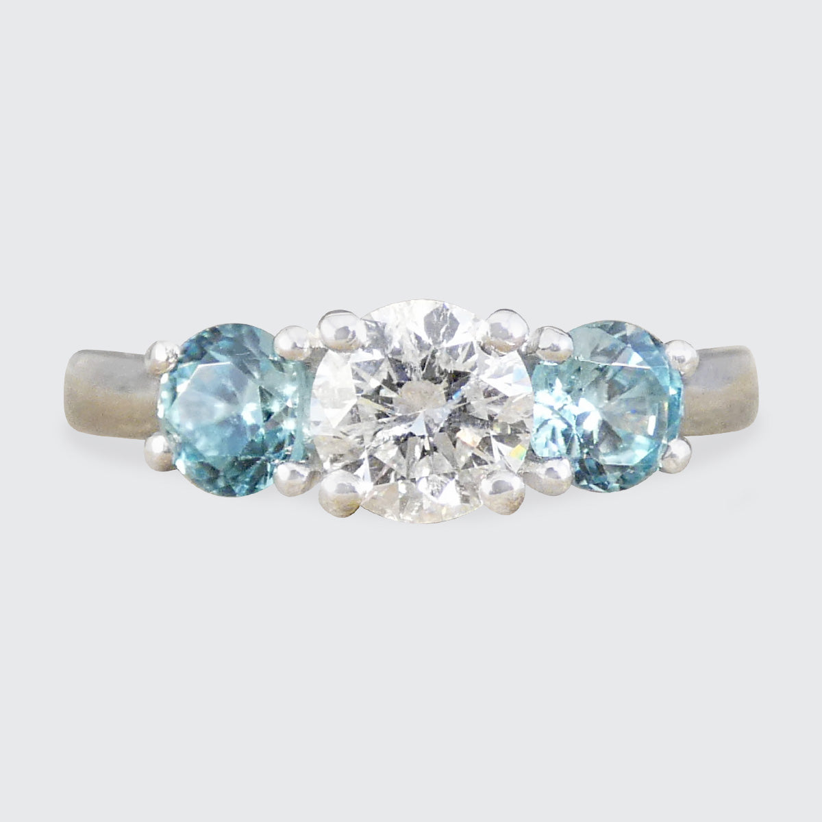 A platinum three-stone ring featuring a round brilliant-cut center diamond flanked by two oval light blue zircons, set in a platinum band.