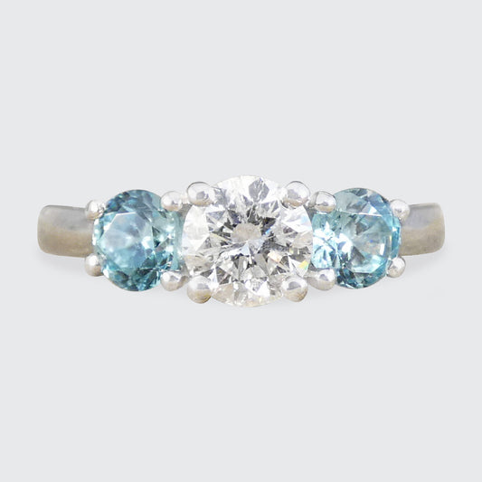 A platinum three-stone ring featuring a round brilliant-cut center diamond flanked by two oval light blue zircons, set in a platinum band.