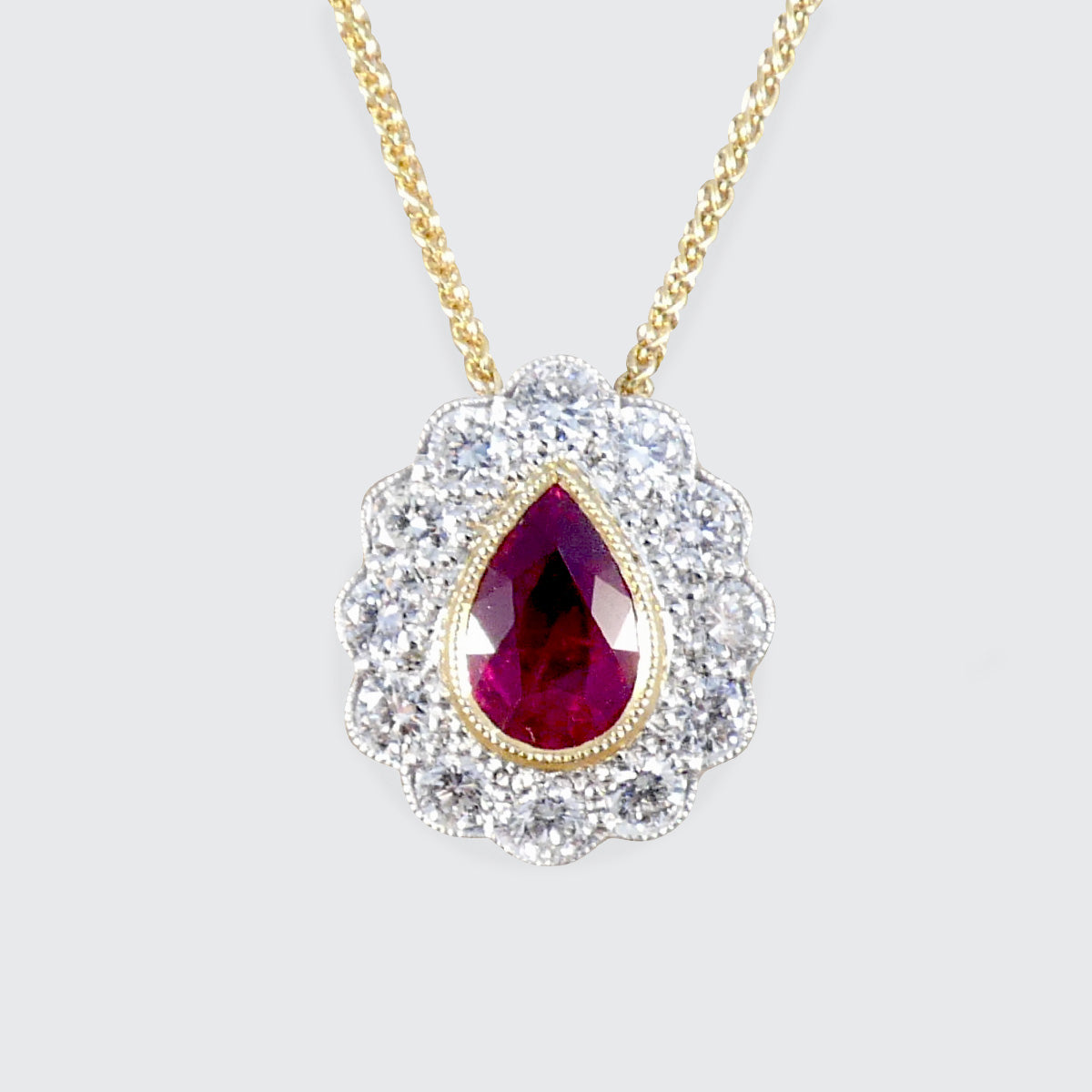Gold necklace with a teardrop-shaped ruby pendant on a light gray background